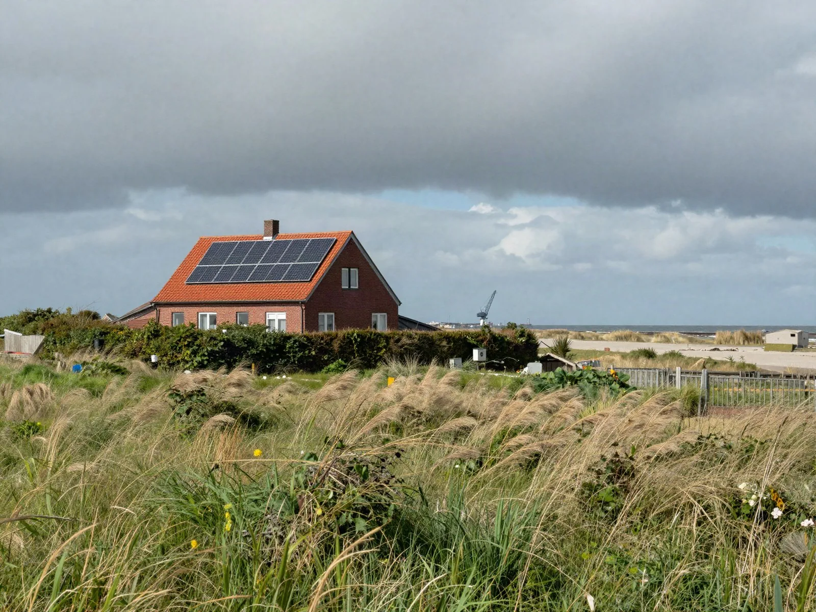 Elektriker Bremerhaven – Anlage anmelden Elektriker Bremerhaven: Backsteinhaus mit Photovoltaik hinter dem Deich an der Küste